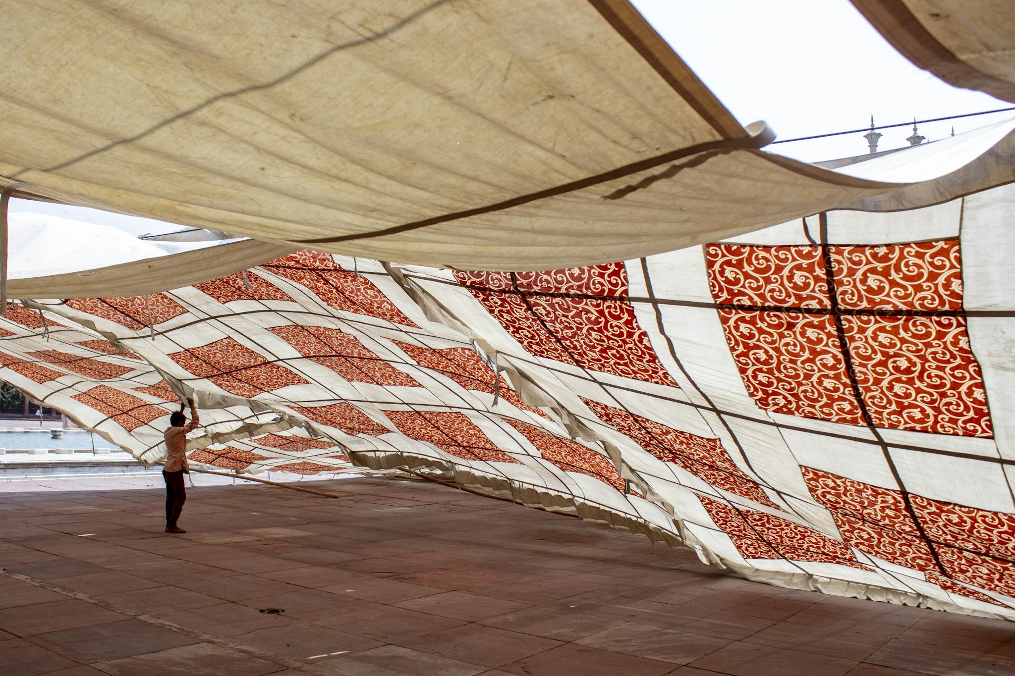 A person adjusting a large decorative canopy with red patterns in an outdoor space.