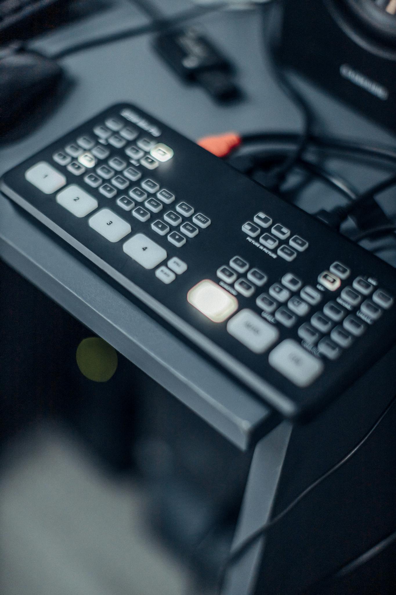 Close-up of a professional video switcher with illuminated control buttons on a desk in a studio setting.